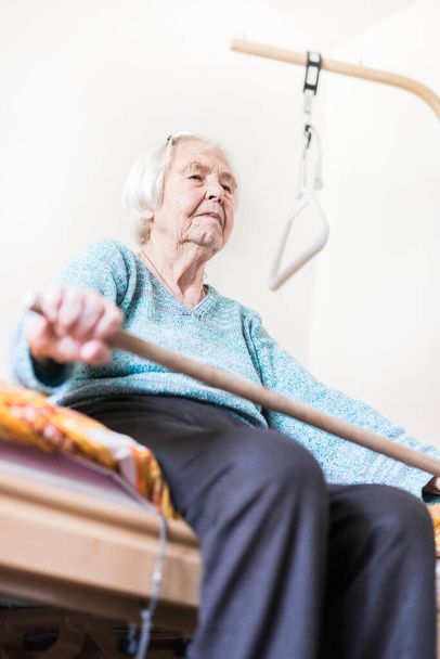 Ältere 96-jährige Frau übt mit einem Stock auf ihrem Bad sitzend. - Foto, Bild
