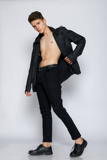 Young muscular man in a black jacket and jeans. young handsome man, leather jacked on naked torso, emotional posing, white background, modern guy, lifestyle people concept - Foto, immagini