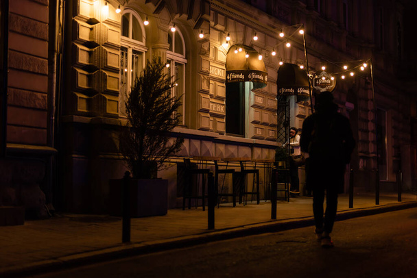 LVIV, UKRAINE - OCTOBER 23, 2019: man walking on street near building with light bulbs  - Foto, imagen