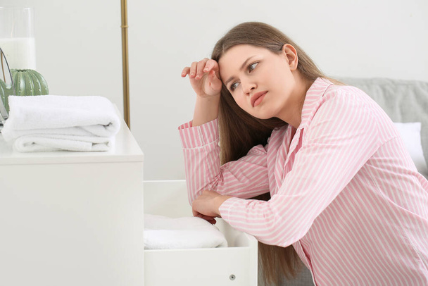 Tired young woman putting clean laundry in chest of drawers - Fotó, kép