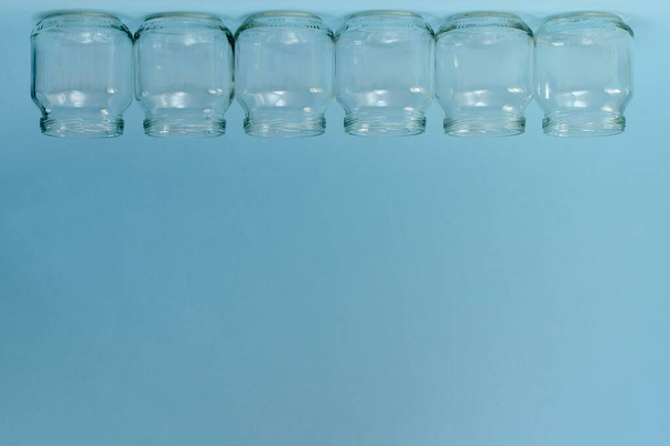 A horizontal row of six transparent inverted jars at the top of the frame on a blue free background. - Fotografie, Obrázek
