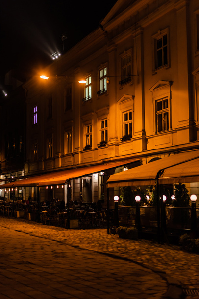 темная улица и силуэт людей, сидящих в кафе с террасой
  - Фото, изображение