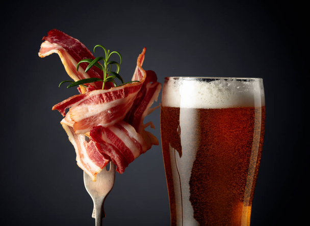Beer and slices of fried bacon garnished with rosemary.  - Фото, зображення