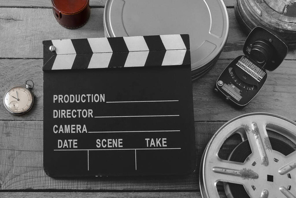 Schwarzweiße Klapptafel, Filmrollen, Taschenuhr und Belichtungsmesser, aufgenommen von oben auf einem Holzbrett - Foto, Bild