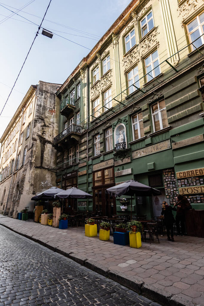 LVIV, UKRAINE - OCTOBER 23, 2019: street cafe with plants in flowerpots near old house with latin lettering  - Fotó, kép
