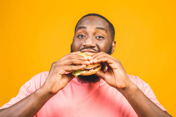 Young african american man eating hamburger isolated over yellow background. - Valokuva, kuva
