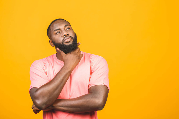 Denkende zwarte Afro-Amerikaanse man met serieuze expressie kijken, poseren geïsoleerd tegen gele achtergrond.  - Foto, afbeelding