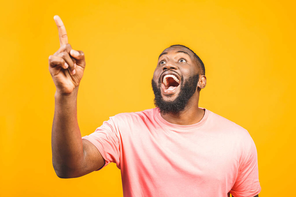 Porträt eines glücklichen jungen, gut aussehenden afroamerikanischen Mannes mit lässig lächelndem Gesicht, der mit dem Finger zur Seite zeigt, mit aufgeregtem Gesichtsausdruck in die Kamera blickt - Foto, Bild