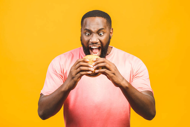 Jeune homme afro-américain manger hamburger isolé sur fond jaune
. - Photo, image