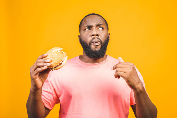 Junger afrikanisch-amerikanischer Mann isst Hamburger isoliert über gelbem Hintergrund. - Foto, Bild