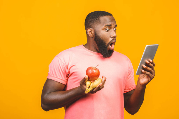 Koncepcja diety. Zdrowy, afrykański czarny mężczyzna trzymający owoce na żółtym tle. Korzystanie z tabletu fo przepis wyszukiwania.  - Zdjęcie, obraz