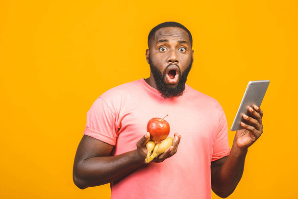 Diet concept. Healthy african american black man holding fruits isolated against yellow background. Using tablet fo searching recipe.  - Photo, image