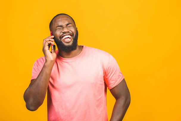 Man on the phone. Cheerful black man talking on the mobile phone and smiling while standing isolated on yellow background.  - Foto, afbeelding
