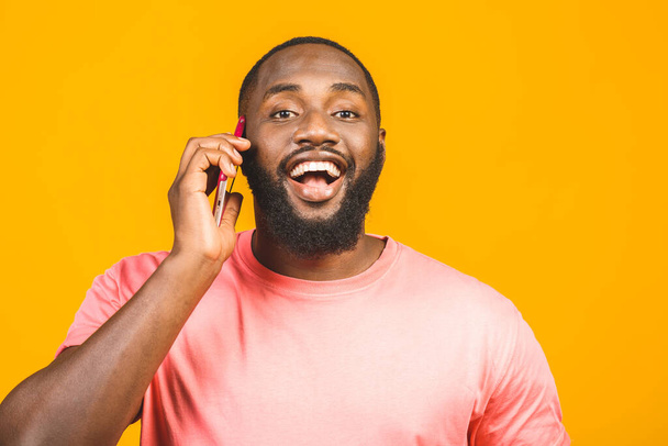 Ο άνθρωπος στο τηλέφωνο. Χαρούμενος μαύρος άντρας που μιλάει στο κινητό και χαμογελάει ενώ στέκεται απομονωμένος σε κίτρινο φόντο.  - Φωτογραφία, εικόνα