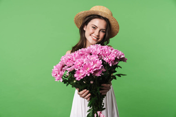 Image of cheerful pretty woman in straw hat smiling and holding flowers isolated over green background - Fotoğraf, Görsel