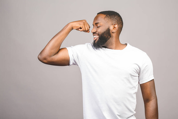 Retrato de cerca de un joven afroamericano feliz flexionando el músculo bíceps aislado sobre fondo gris.  - Foto, Imagen