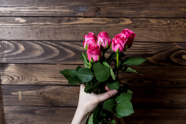 main féminine tient un bouquet de roses rouges sur un fond en bois
. - Photo, image