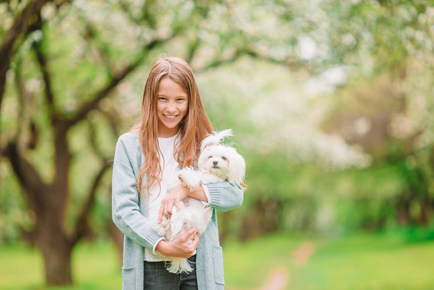 Маленькая улыбающаяся девочка играет и обнимает щенка в парке - Фото, изображение