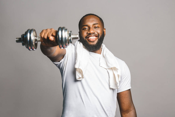 Concepto fitness. Retrato de un hombre negro afroamericano feliz con mancuernas aisladas sobre fondo gris
. - Foto, imagen