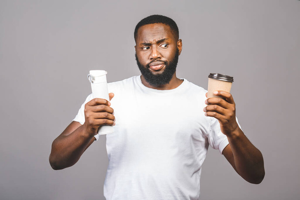 Zero conceito de desperdício. Jovem afro-americano fazendo escolha entre xícara de café e reciclar um pé sobre fundo cinza isolado
. - Foto, Imagem