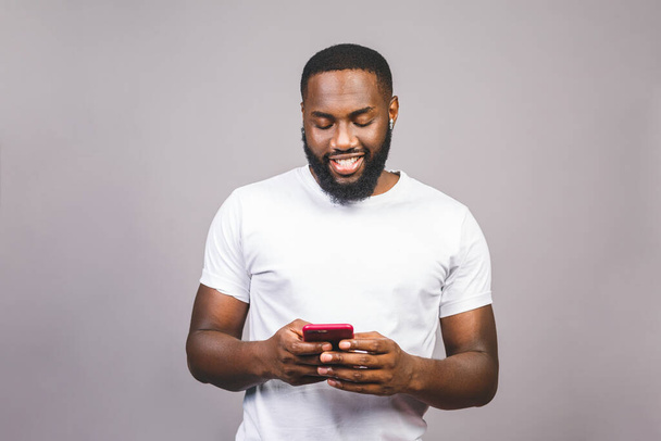 Portrait of handsome excited cheerful joyful delightful curious guy wearing casual sending and getting messages to his lover isolated against grey background. Using phone. - Photo, Image