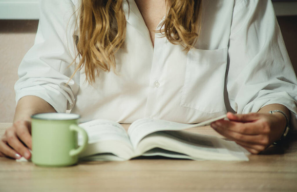 Kız kitap okuyor ve yakın planda kahve içiyor. - Fotoğraf, Görsel