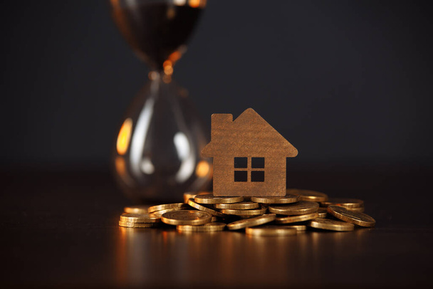 Bozuk para ve kum saatinin üzerindeki ev modeli. Yatırım gayrimenkul kavramı - Fotoğraf, Görsel