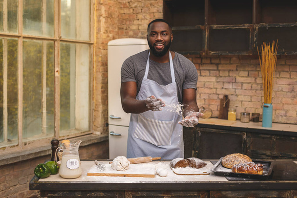 Bakproces. Vrolijke donkere huid Afro-Amerikaanse man draagt schort, kneedt deeg met groot enthousiasme, tevreden te zijn met de lof van de chef-kok voor inspanning en hard werken in restaurant. - Foto, afbeelding