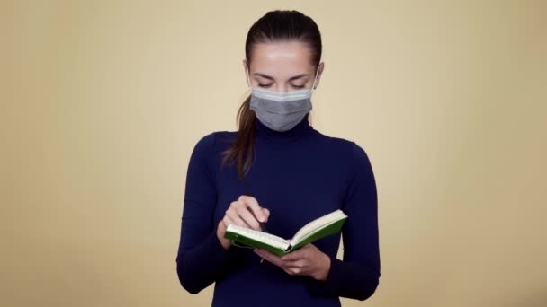 Woman in protective medical mask writes in diary, shows inscription COVID 19 - Video