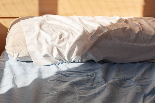 目覚めのコンセプト:朝の窓の光に照らされたシートにしわがある未加工のベッドの枕 - 写真・画像