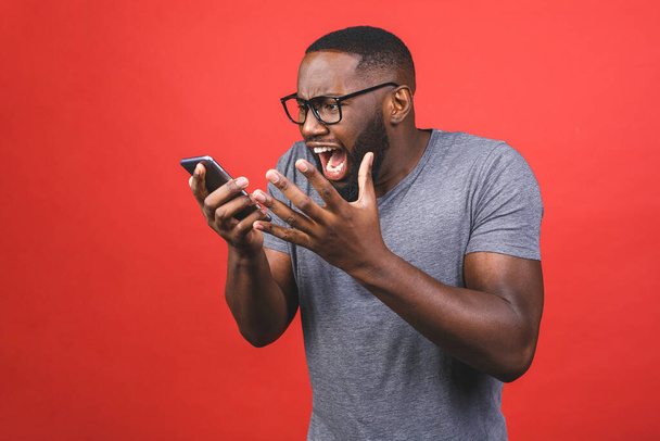 Giovane uomo afroamericano utilizzando smartphone stressato, scioccato con vergogna e faccia a sorpresa, arrabbiato e frustrato. Paura e sconvolgimento per errore. Isolato su sfondo rosso
. - Foto, immagini