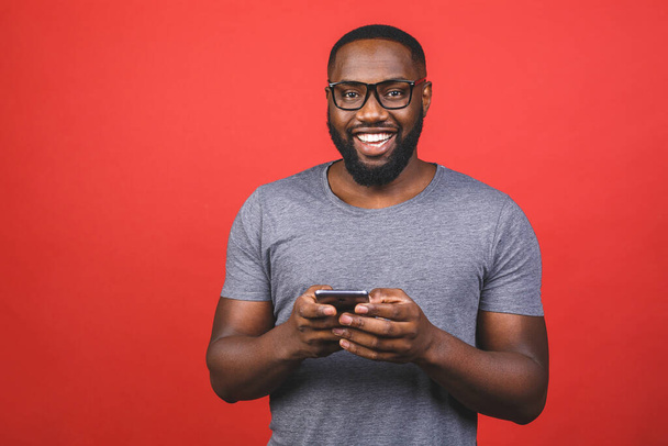 Porträt eines gutaussehenden aufgeregten fröhlichen freudigen entzückenden afrikanisch-amerikanischen Typen, der lässig vor rotem Hintergrund Nachrichten an seine Geliebte sendet und erhält. Telefonieren.  - Foto, Bild