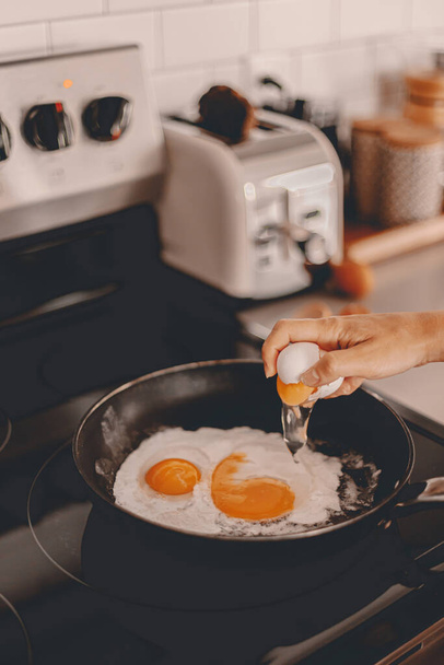 朝食の準備。朝ご飯を作る。平日のルーティン。家族のために働く前に料理を作る。鍋に卵をクラック.家庭生活。夫とブランチ。ストーブトースター。選択的焦点 - 写真・画像