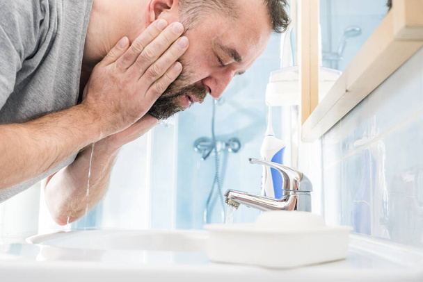 Hombre salpicando agua en su cara, lavándose, cuidando de la higiene personal. Sentirse fresco por la mañana - Foto, Imagen