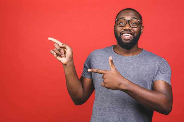 Afro-Amerikaanse man over geïsoleerde rode achtergrond verbaasd en glimlachend naar de camera terwijl presenteren met de hand en wijzen met de vinger. - Foto, afbeelding