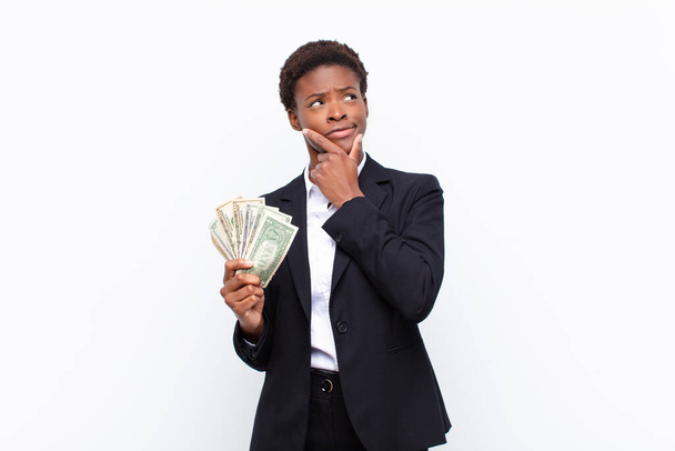 young pretty black womanthinking, feeling doubtful and confused, with different options, wondering which decision to make with dollar banknotes - Фото, изображение