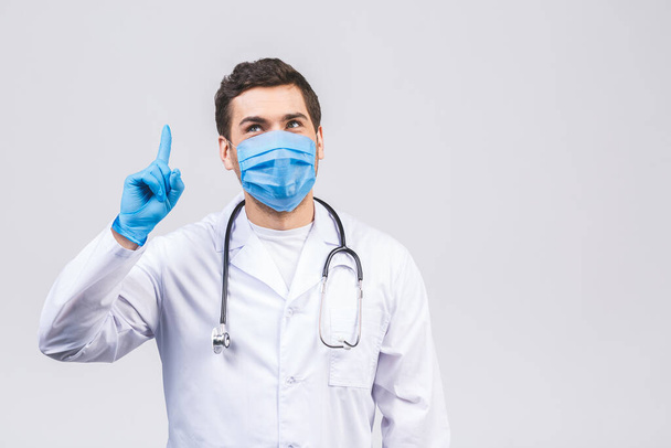 Γιατρός άνθρωπος σε ιατρική ρόμπα αποστειρωμένα γάντια μάσκα προσώπου απομονώνονται σε λευκό φόντο. Επιδημική πανδημία coronavirus 2019-ncov sars covid-19 ιό της γρίπης. Δείχνοντας το δάχτυλο προς τα πάνω. - Φωτογραφία, εικόνα