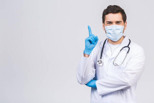 Доктор чоловік в медичній сукні стерильні маски для обличчя ізольовані на білому тлі. Епідемічна пандемія коронавірусу 2019-московський синдром ковідо-19 грипу. Наведення пальця в сторону вгору
. - Фото, зображення