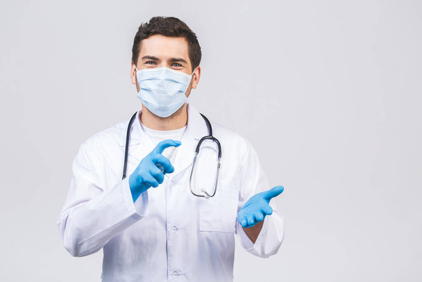 Доктор человек в мантии маска перчатки изолированы на белом фоне. Эпидемический пандемический коронавирус 2019 года - вирус сарс ковид-19 гриппа. Бутылка с антибактериальным антибактериальным дезинфицирующим средством
. - Фото, изображение