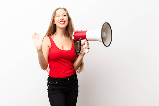 yound blonde woman looking happy and pleasantly surprised, excited with a fascinated and shocked expression holding a megaphone - Φωτογραφία, εικόνα