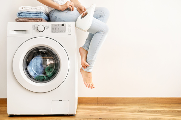 Young woman with washing gel sitting on washing machine - Zdjęcie, obraz