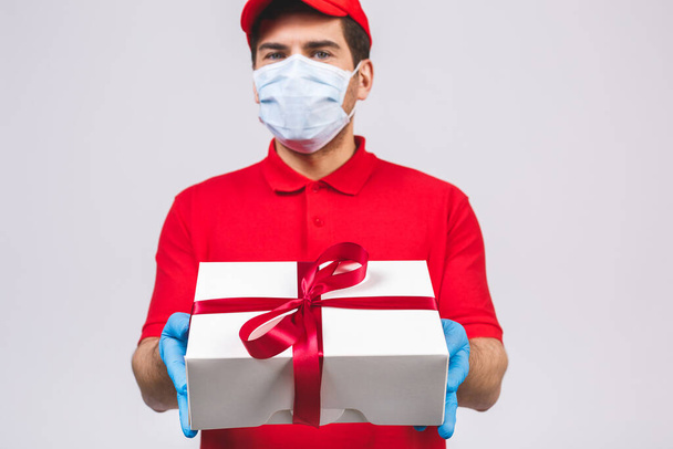 Delivery man employee in red cap blank t-shirt uniform face mask gloves hold empty cardboard box isolated on white background. Service quarantine pandemic coronavirus virus 2019-ncov concept. - Photo, image