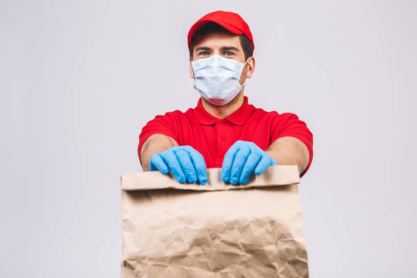 赤いキャップの空のTシャツの制服顔マスク手袋の配達人の従業員は白い背景に隔離された空の段ボール箱を保持します。サービス検疫パンデミックコロナウイルス2019-ncovコンセプト. - 写真・画像