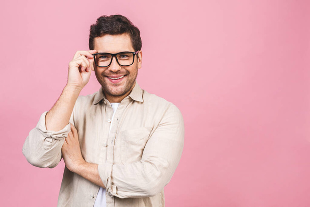 Un retrato de joven hombre de negocios guapo sonriente en camisa casual aislado sobre fondo rosa tocando sus gafas
. - Foto, imagen