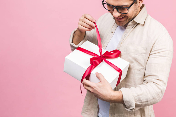 Концепция праздника. Портрет молодого человека, открывающего подарочную коробку на розовом фоне
. - Фото, изображение