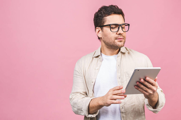 Jovem atraente feliz de pé e usando computador tablet isolado sobre fundo rosa
. - Foto, Imagem