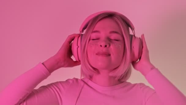A woman in a pink neon light listens to music on headphones enjoys and dancing closing her eyes.  Smooth dance.  - Metraje, vídeo