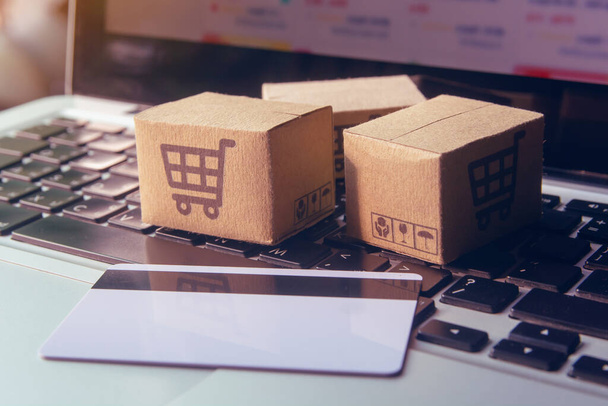 Online shopping - Paper cartons or parcel with a shopping cart logo and credit card on a laptop keyboard. Shopping service on The online web and offers home delivery - Zdjęcie, obraz