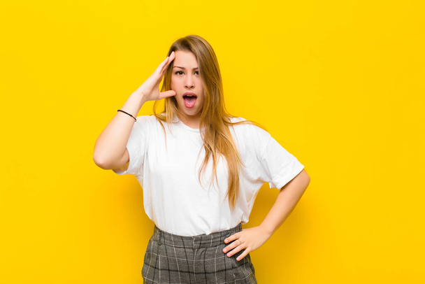 young blonde woman looking happy, astonished and surprised, smiling and realizing amazing and incredible good news against orange wall - Foto, afbeelding