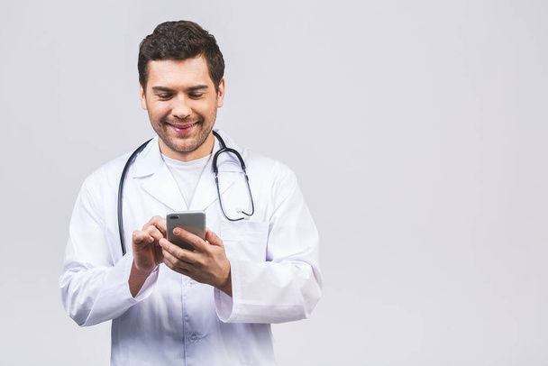 男性医師の手を携帯電話を使用して、携帯電話で手。白いコートの男性医師は、白い背景に隔離された現代のスマートフォンデバイスを使用しています.  - 写真・画像